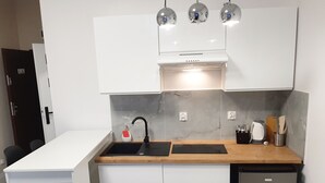 Una cocina compacta con gabinetes blancos, un lavamanos negro y un lavavajillas integrado.
