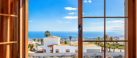 A view through a wooden-framed window with a clear sky and distant ocean.