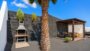 Een terras met een stenen muur, een barbecue, een palmboom en een overdekt zitgedeelte.