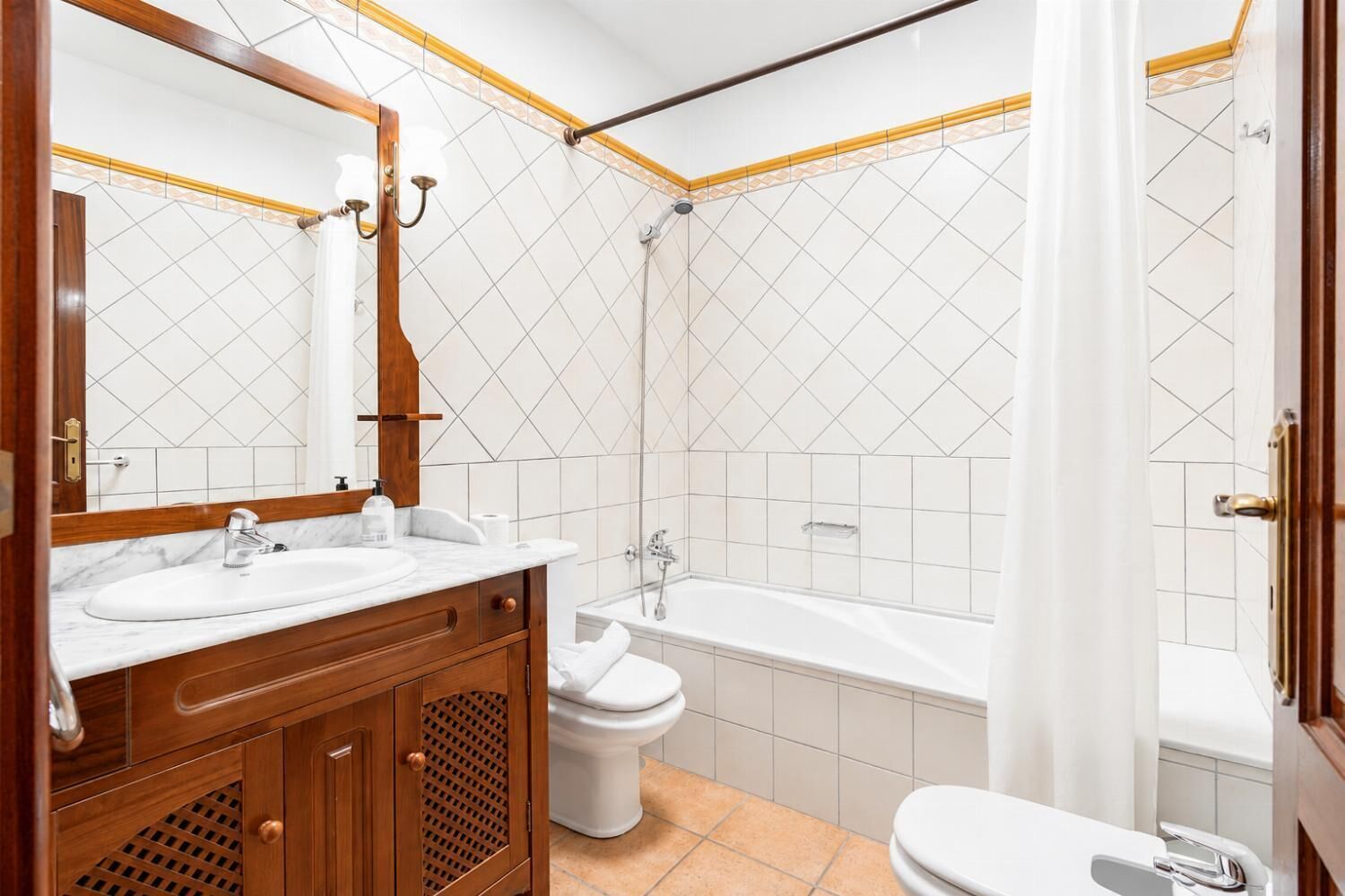 Een badkamer met een houten wastafelmeubel, een witte wastafel, toilet en bad.