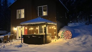 Una casa de dos pisos con un área de estar techada al aire libre, rodeada de nieve.