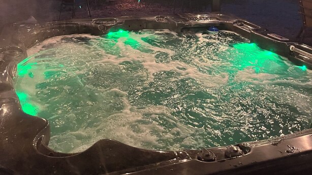 Un jacuzzi con iluminación verde, rodeado por una zona cubierta con vigas de metal y luces colgantes.