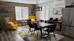 Una cocina moderna con comedor, que incluye suelo de madera, un sillón amarillo, una mesa de comedor con sillas y una encimera con electrodomésticos.