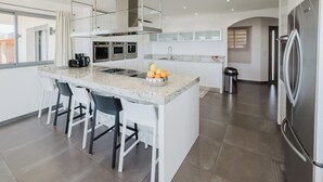 A modern kitchen with a central island, bar stools, stainless steel appliances, and a large refrigerator. - Villa de Prestige 460m2, Pinarello, Magnifique vue Mer, Piscine Chauffée (Porto-Vecchio)