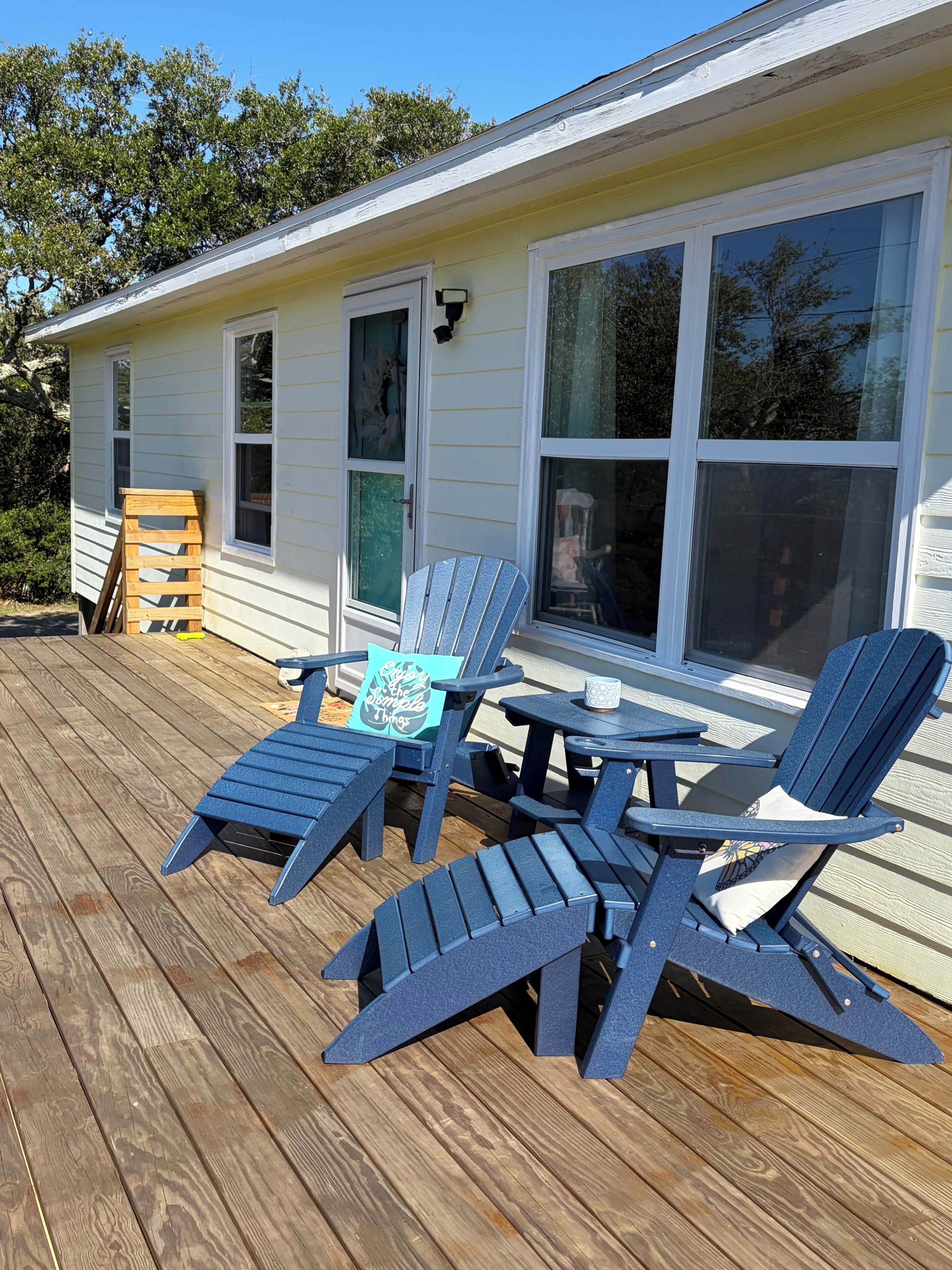Une terrasse avec des fauteuils Adirondack et une petite table, une maison avec de grandes fenêtres et une porte.