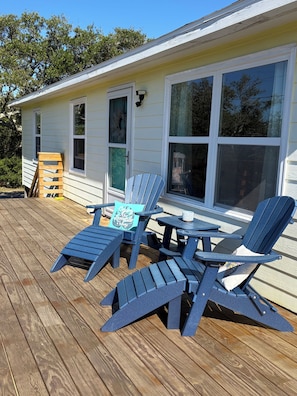 Une terrasse avec des fauteuils Adirondack et une petite table, une maison avec de grandes fenêtres et une porte.
