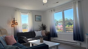 Een woonkamer met een plafondventilator, een bank, een bijzettafeltje en uitzicht op de omgeving.