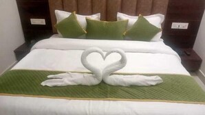A hotel room with a neatly made bed, green and white bedding, and a swan-shaped towel arrangement. - Epic Star Hotels and Resorts Amritsar (Amritsar)