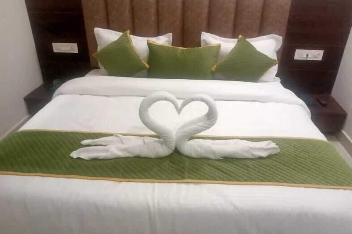 A hotel room with a neatly made bed, green and white bedding, and a swan-shaped towel arrangement.