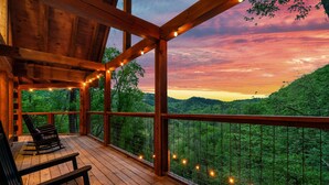 A wooden deck with string lights, a rocking chair, and a view of a forested landscape. - FreeDollywoodTix,HeatedPool,Luxurious,HotTub,Views (Sevierville)