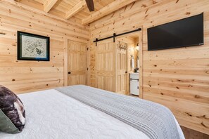 A wooden-paneled room with a bed, a framed map, a sliding door, and a mounted television.