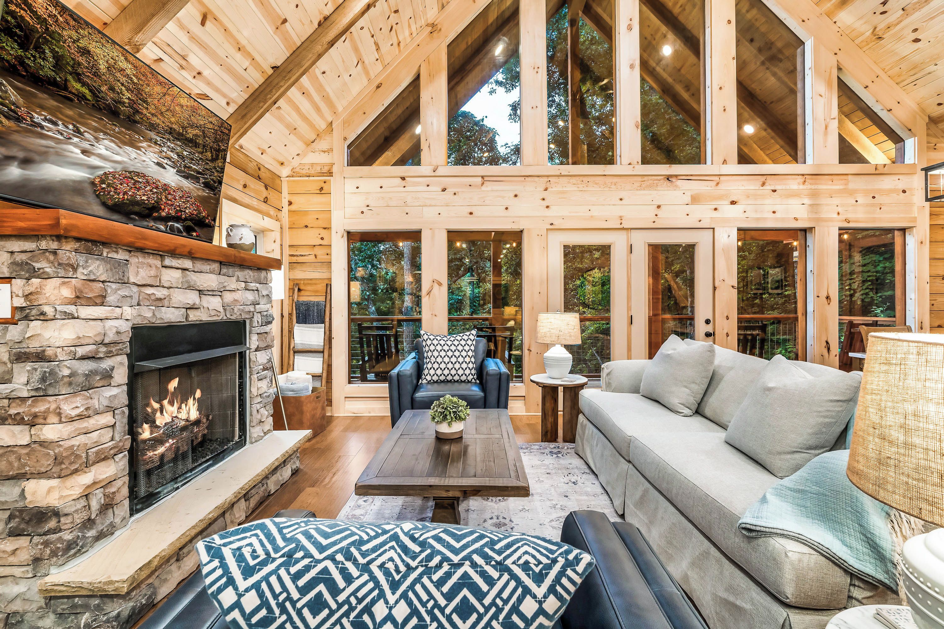 Amplia sala de estar con chimenea de piedra, vigas de madera y ventanas grandes con vistas al exterior.