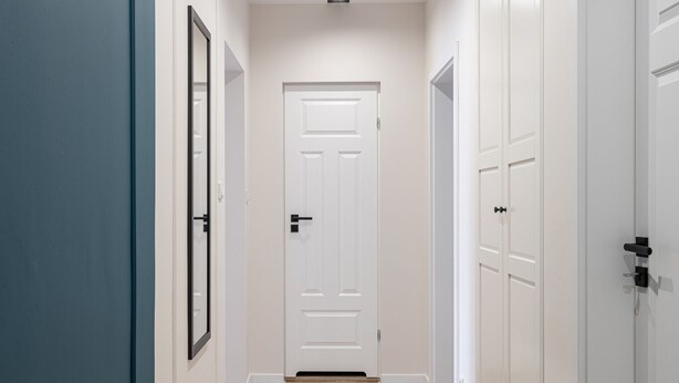 A hallway with a wooden floor, white walls, and a blue door on the left.