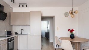 A modern kitchen with a central island, a dining area with a round table and chairs, and a visible hallway leading to another room.