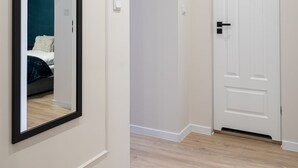 A hallway with a wooden floor, a white door, and a large mirror on the left wall.