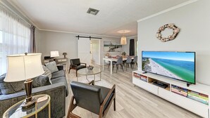 Un salon moderne avec un canapé, une table basse et un téléviseur. Il y a également un coin repas avec des chaises et une table.
