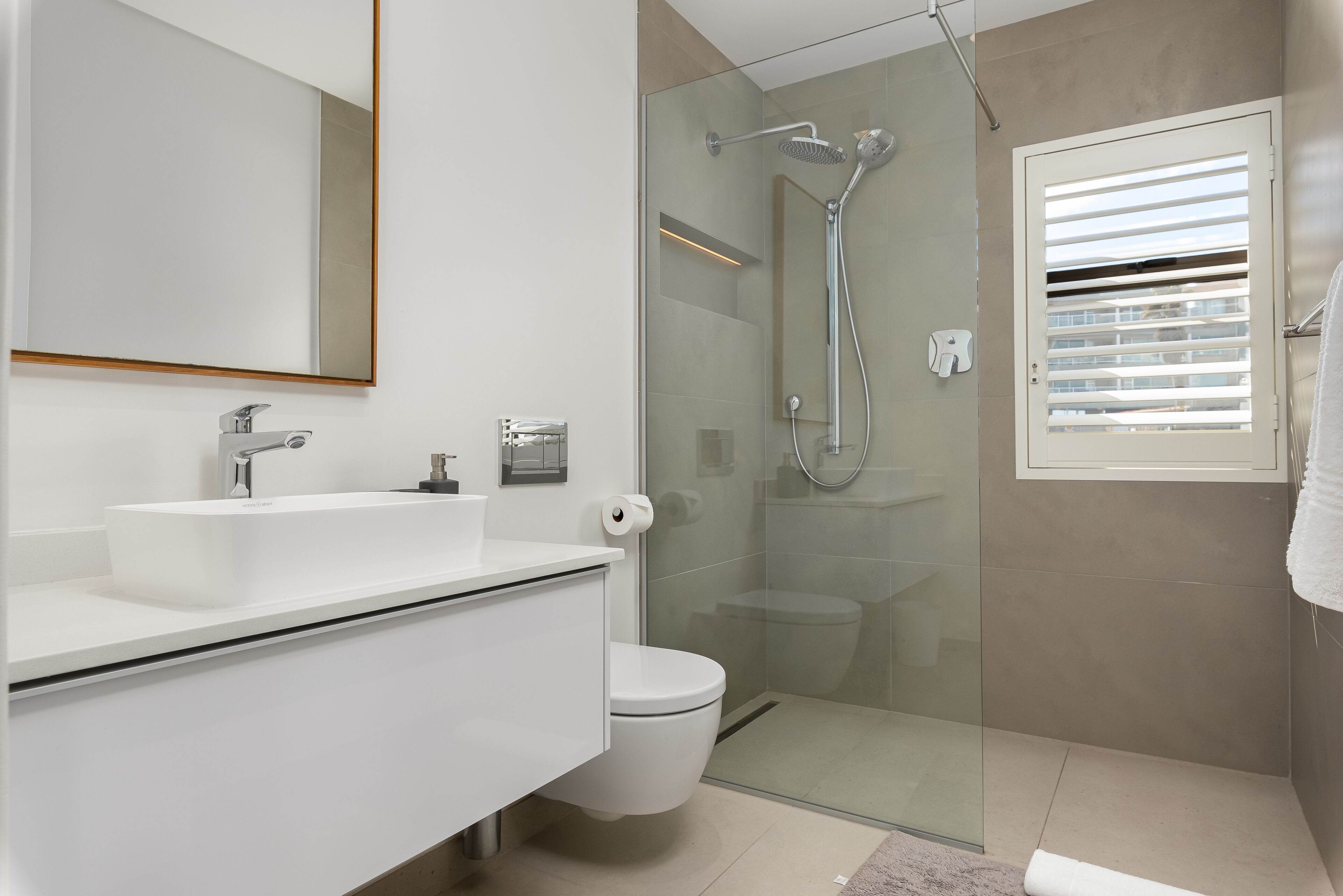 Een moderne badkamer met een glazen douchecabine, een witte wastafel en een toilet.
