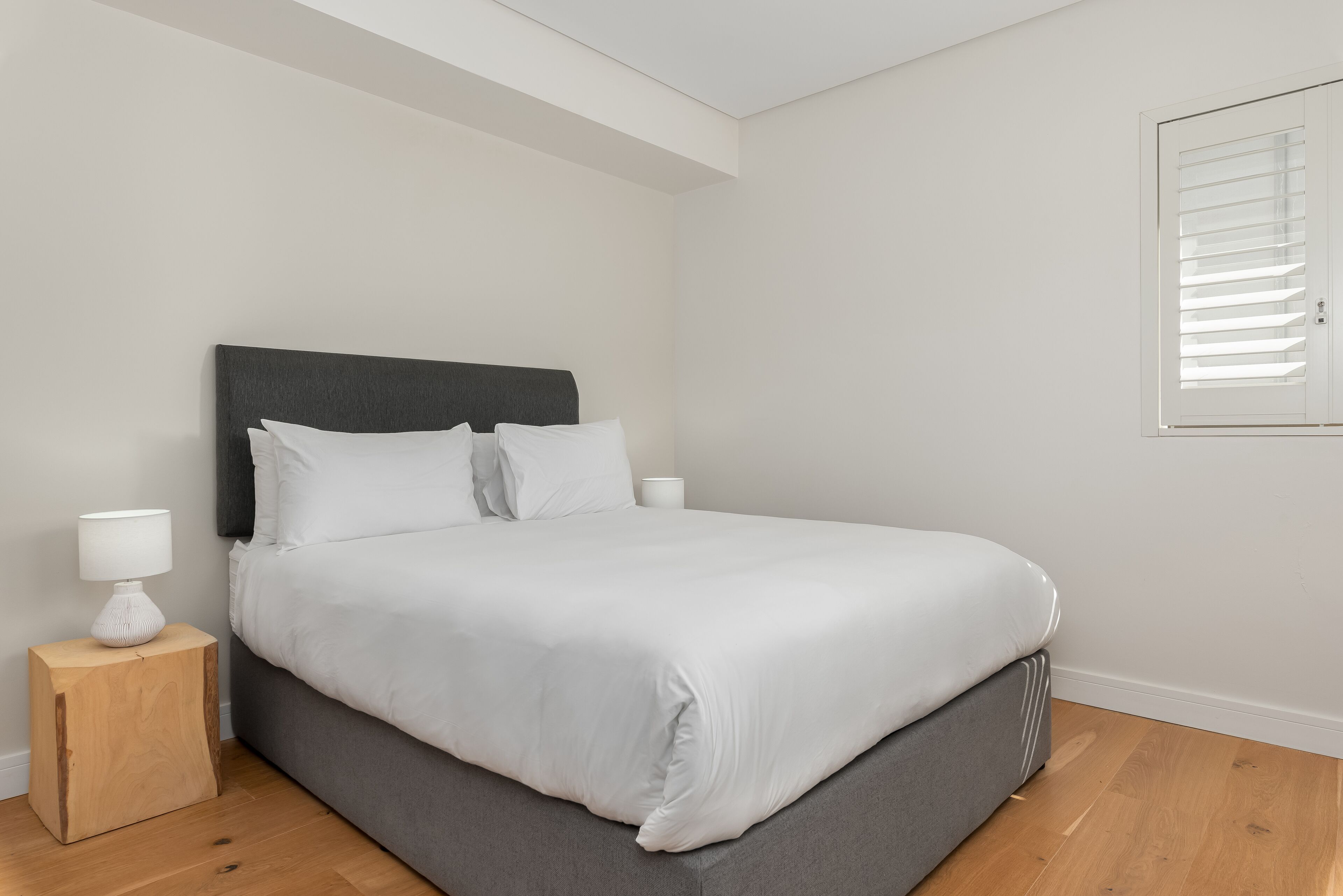 A neatly made bed with white linens, a dark headboard, and a small bedside table with a lamp.