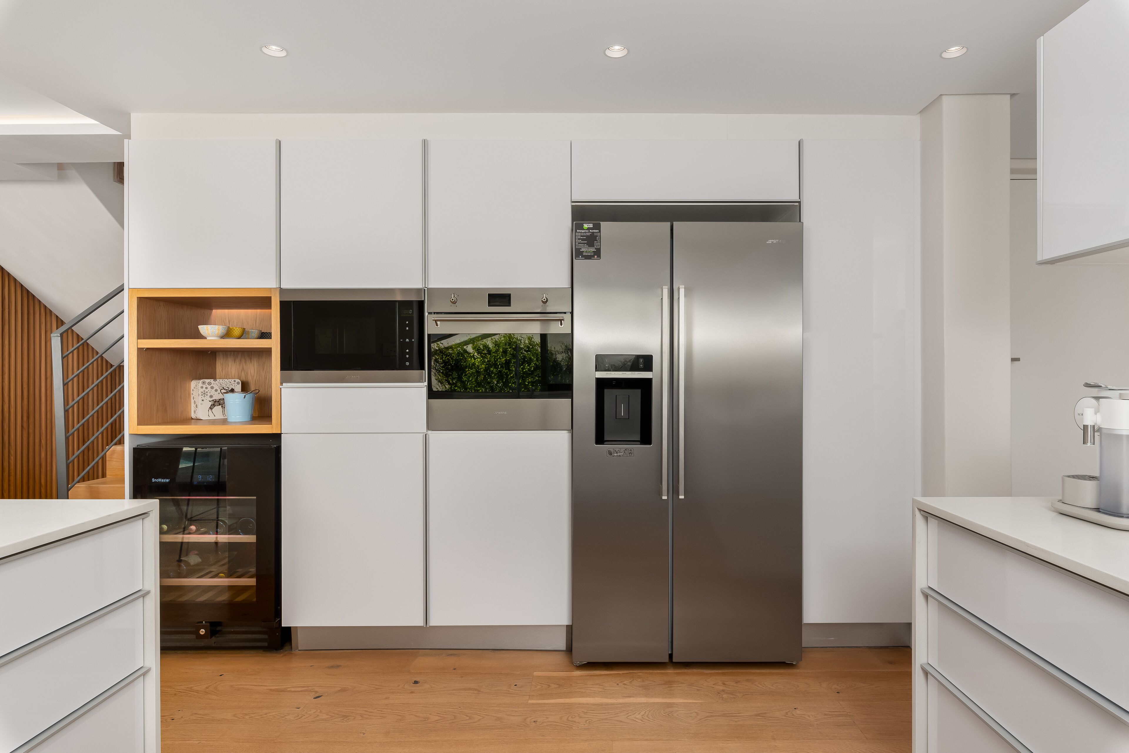 A modern kitchen with white cabinetry, a stainless steel refrigerator, a built-in oven, and a microwave.