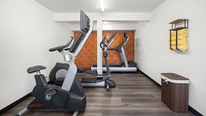 Ein Fitnessraum mit Cardiogeräten, Holzboden und Mülleimer.