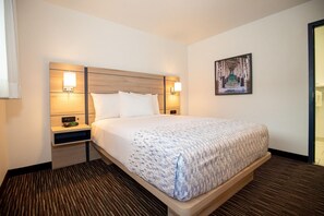 A hotel room with a bed, bedside tables, wall-mounted lamps, a painting, and a door.