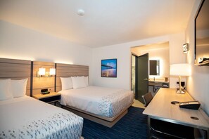 A hotel room with two beds, a desk, a chair, a mirror, and a picture on the wall.