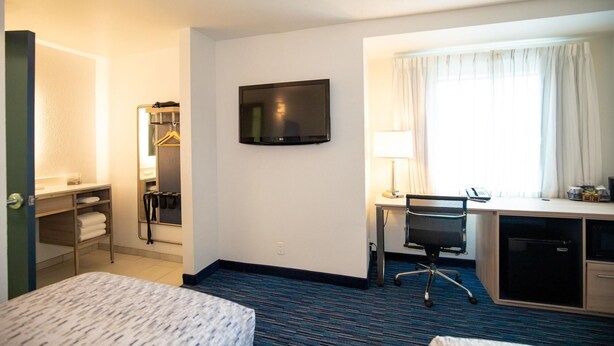 Ein Hotelzimmer mit Bett, Schreibtisch, Stuhl, Fernseher und einem Fenster mit Vorhängen.