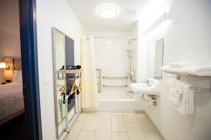 Un baño de hotel con ducha, lavamanos, espejo y toallero.