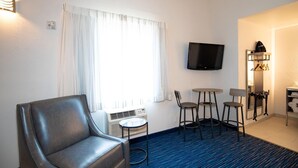 Ein Hotelzimmer mit Ledersessel, kleinem Tisch, zwei Stühlen, Fernseher und Spiegel mit Garderobe.
