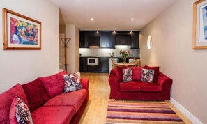 Un espace de vie compact avec deux canapés rouges, un tapis à rayures et une cuisine en arrière-plan.