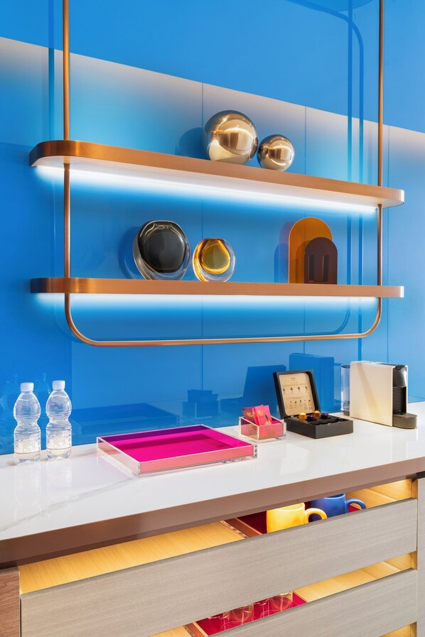 A modern hotel reception desk with a blue and white color scheme, a metallic shelf with decorative items, and a counter with various amenities. - Maqo Changsha  (Changsha)