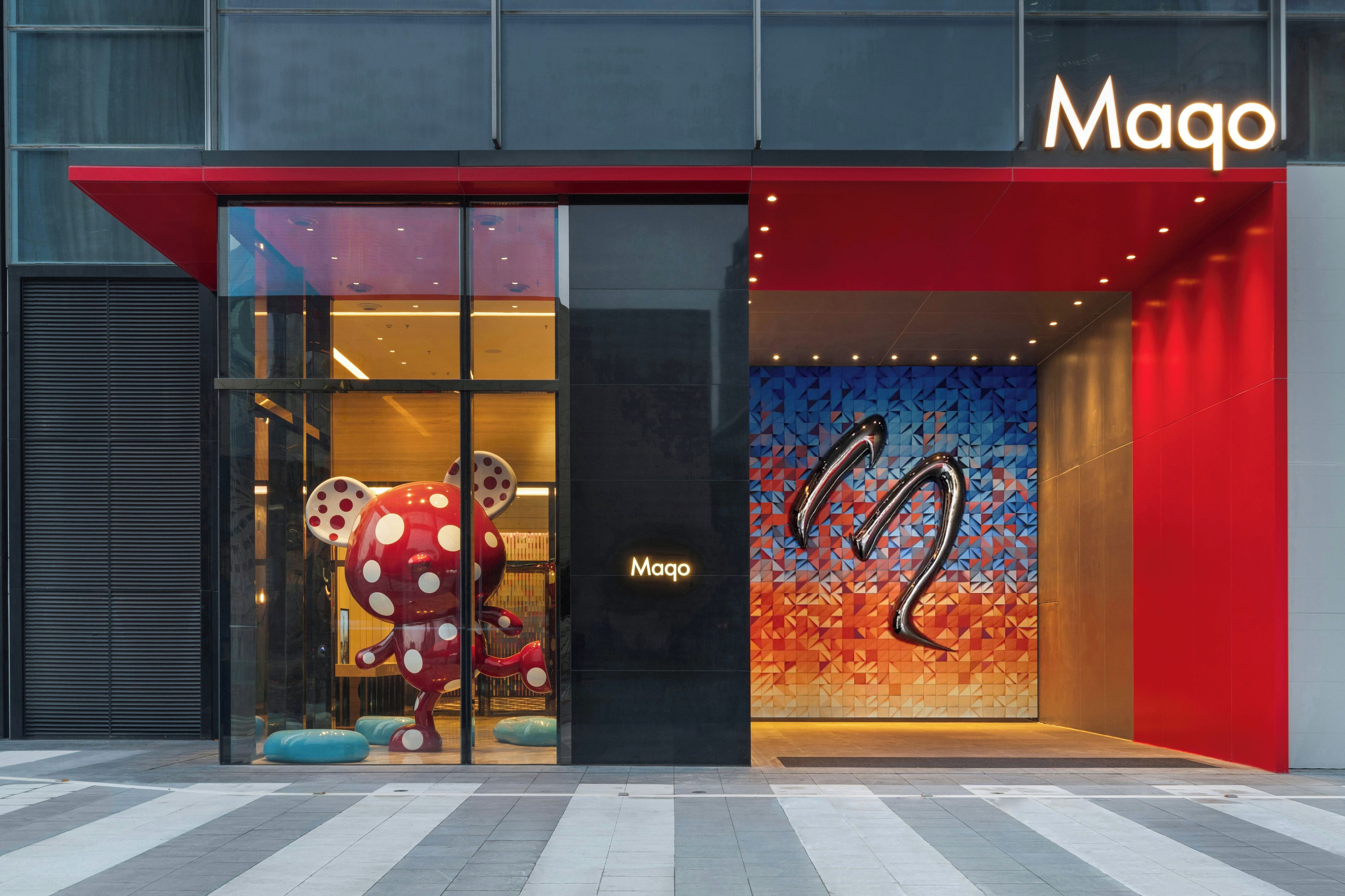 A building entrance with a glass facade, a large red awning, and a logo above the entrance.