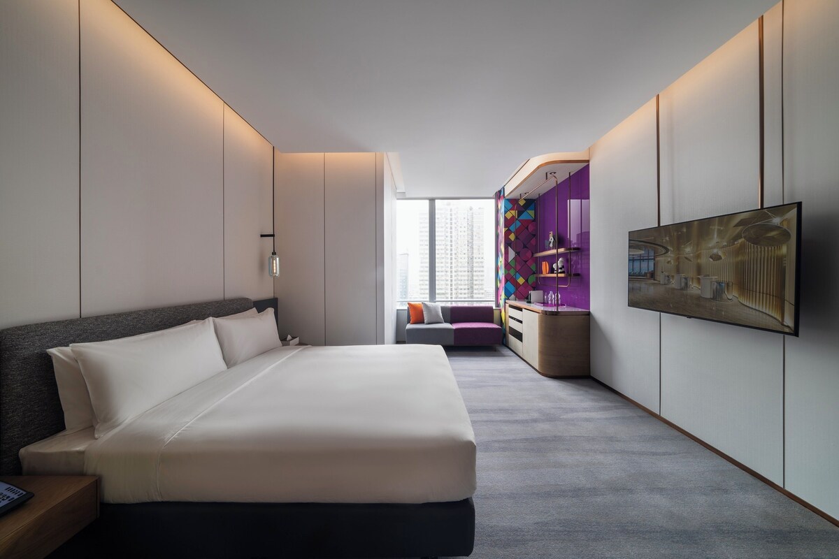 Une chambre d’hôtel moderne dotée d’un grand lit, d’un téléviseur à écran plat et offrant une vue sur la ville grâce à de grandes fenêtres.