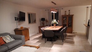 A living room with a sofa, a coffee table, a dining table with chairs, a TV mounted on the wall, and a cabinet. - Villa Rénovée, à 5 Minutes du Centre et D'un Supermarché (Cogolin)
