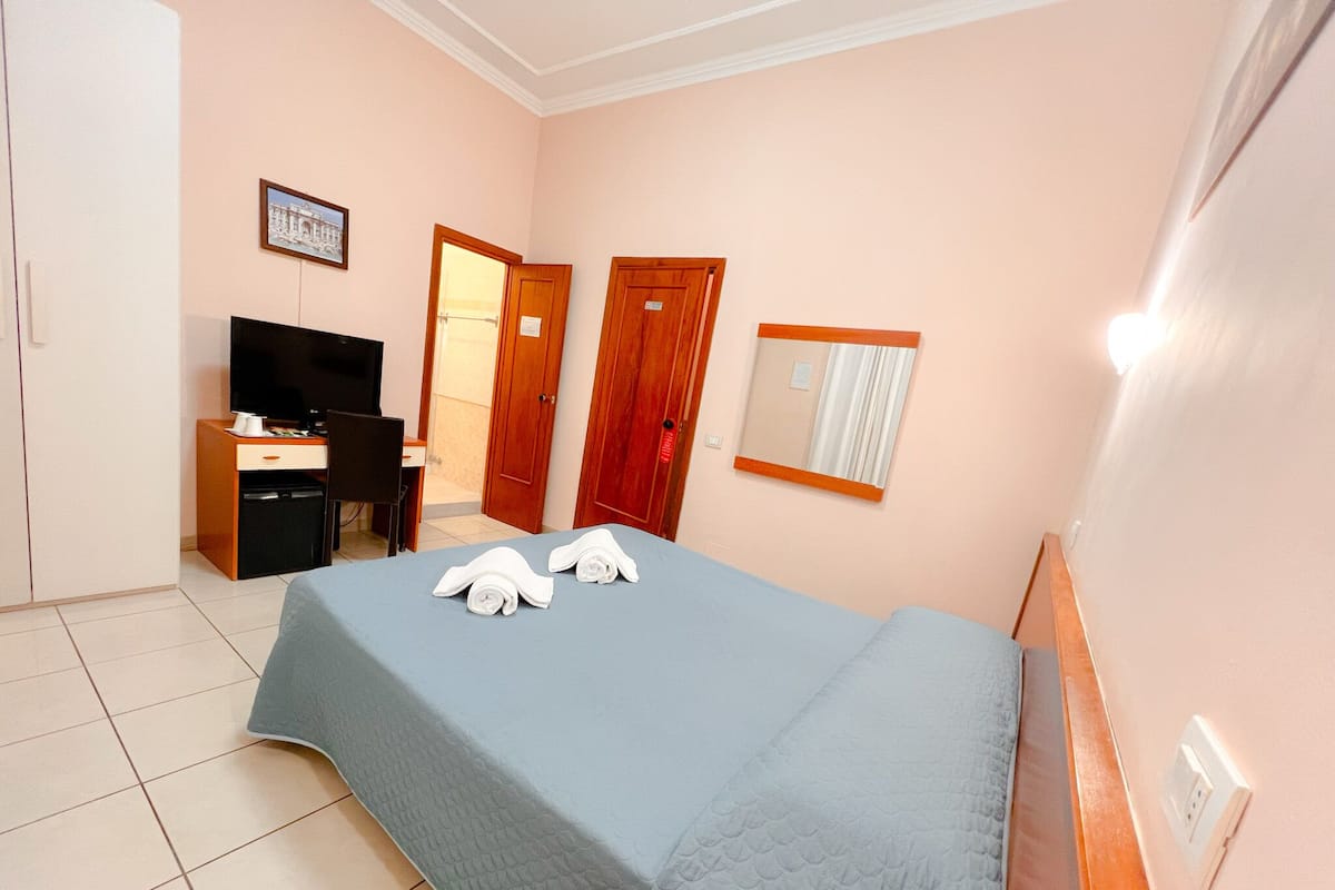 A hotel room with a bed, a desk, a television, and a bathroom door.