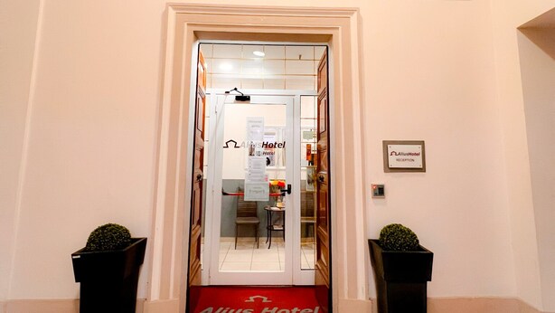 A hotel entrance with a red carpet leading to a reception desk. There are two potted plants on either side of the entrance. - Alius And Freerome Hotel  (Rome)