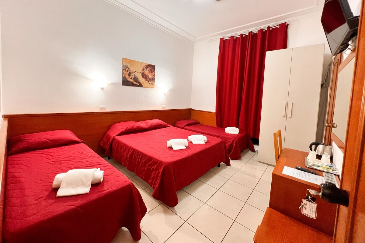 A hotel room with two single beds, a desk with a computer, a TV, and a wardrobe.