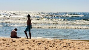A beach with two people, one standing and one sitting, and waves crashing onto the shore. - Spacious lakeview home within minutes of beaches, state parks and shopping. (SPRING LAKE)
