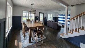 A spacious living area with a wooden dining table, dark wood flooring, and a staircase leading to an upper level. - Spacious lakeview home within minutes of beaches, state parks and shopping. (SPRING LAKE)