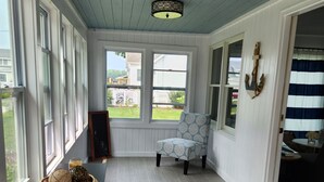 A room with a view of the backyard, a wicker basket on a table, a patterned chair, and a striped curtain. - Spacious lakeview home within minutes of beaches, state parks and shopping. (SPRING LAKE)