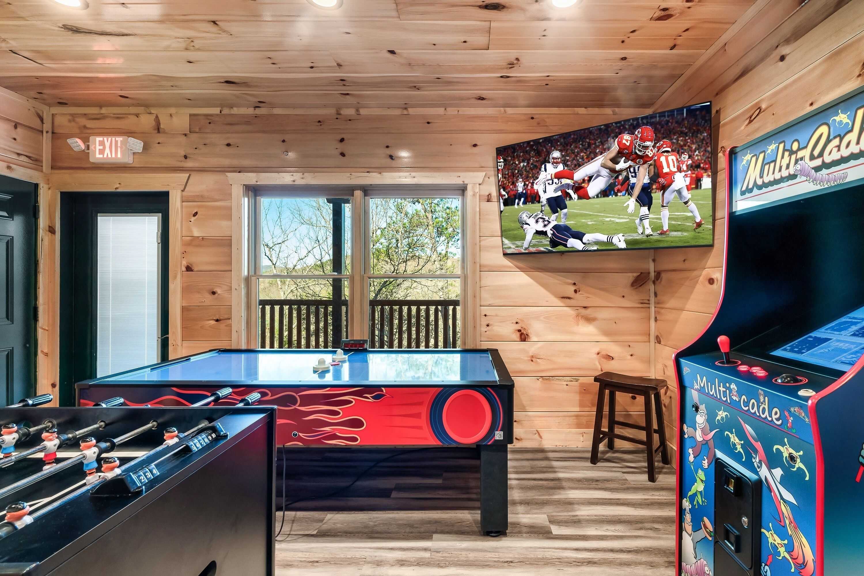 Een kamer met een tafelvoetbaltafel, een televisie waarop een voetbalwedstrijd draait en een Multi-Cade spelautomaat.