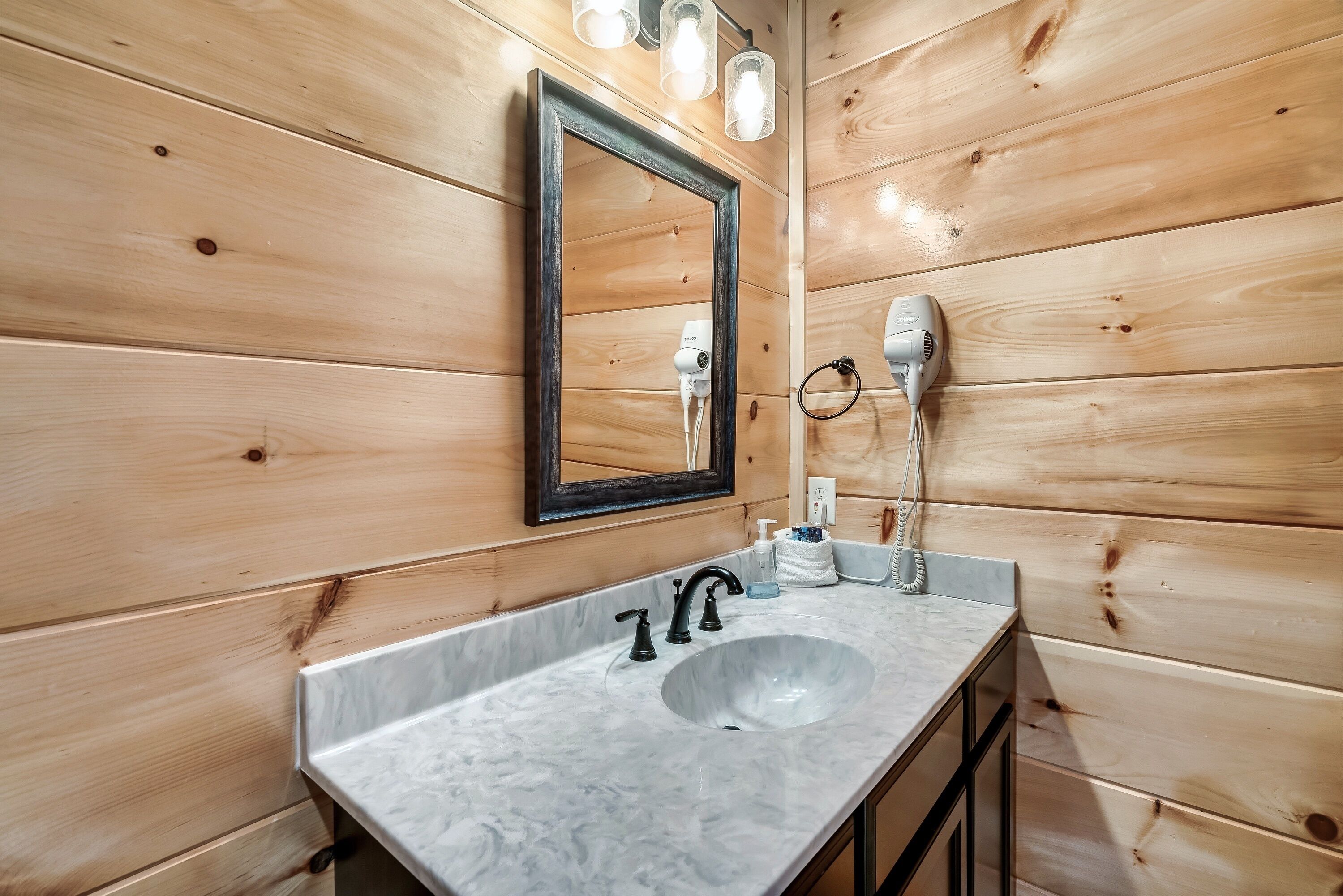 Un baño con pared de madera, lavamanos de mármol, espejo y secador de pelo en la pared.