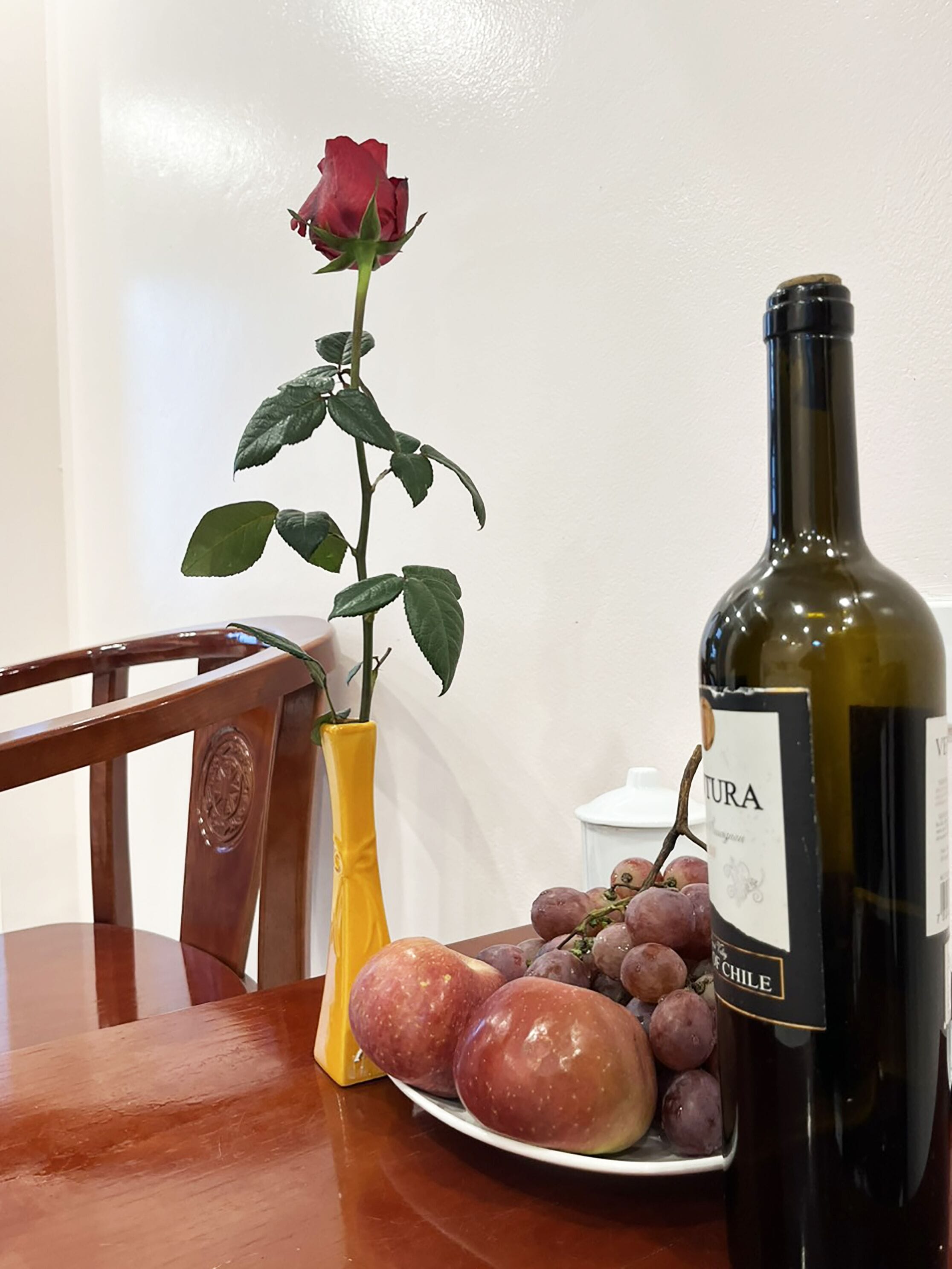 Ein Tisch mit einer Weinflasche, einer Rose und einer Platte Trauben.