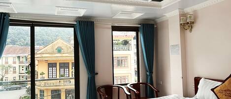 Een hotelkamer met een groot bed, uitzicht op gebouwen en een balkon met blauwe gordijnen.
