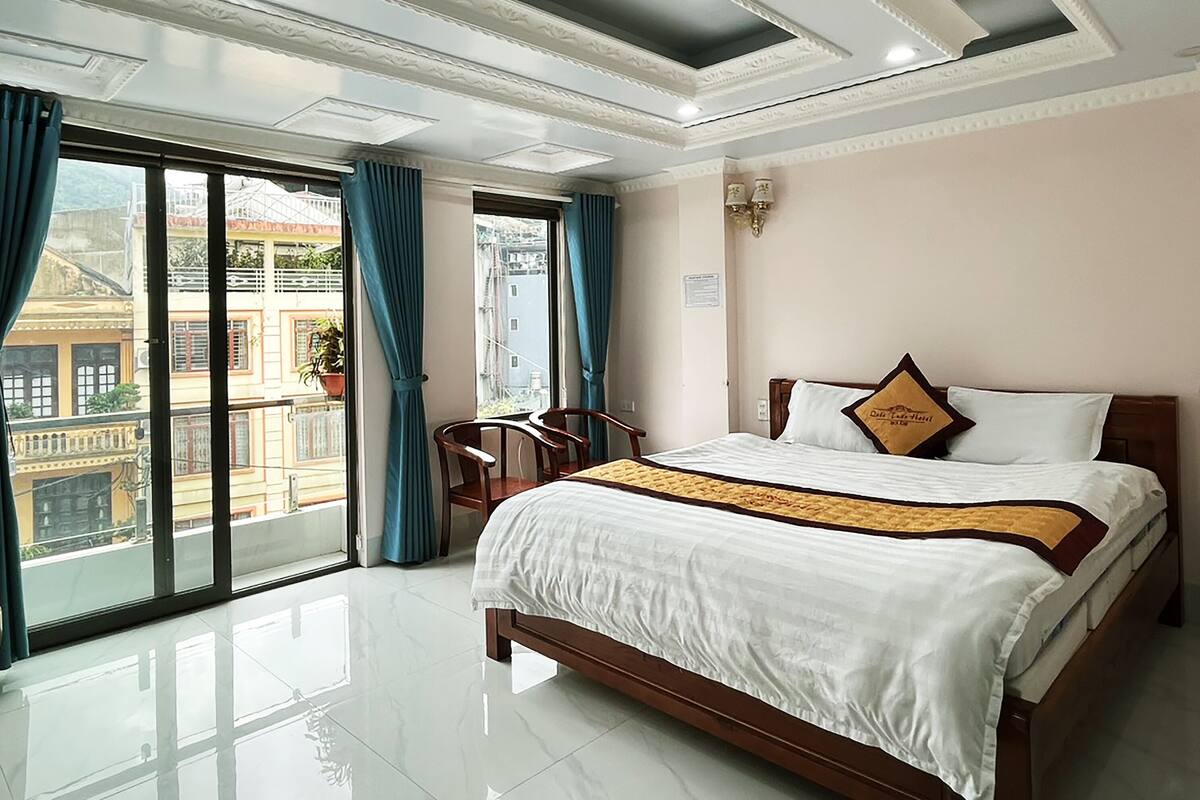 Quarto de hotel com uma cama grande, vista através de uma porta de correr e teto com molduras decorativas.