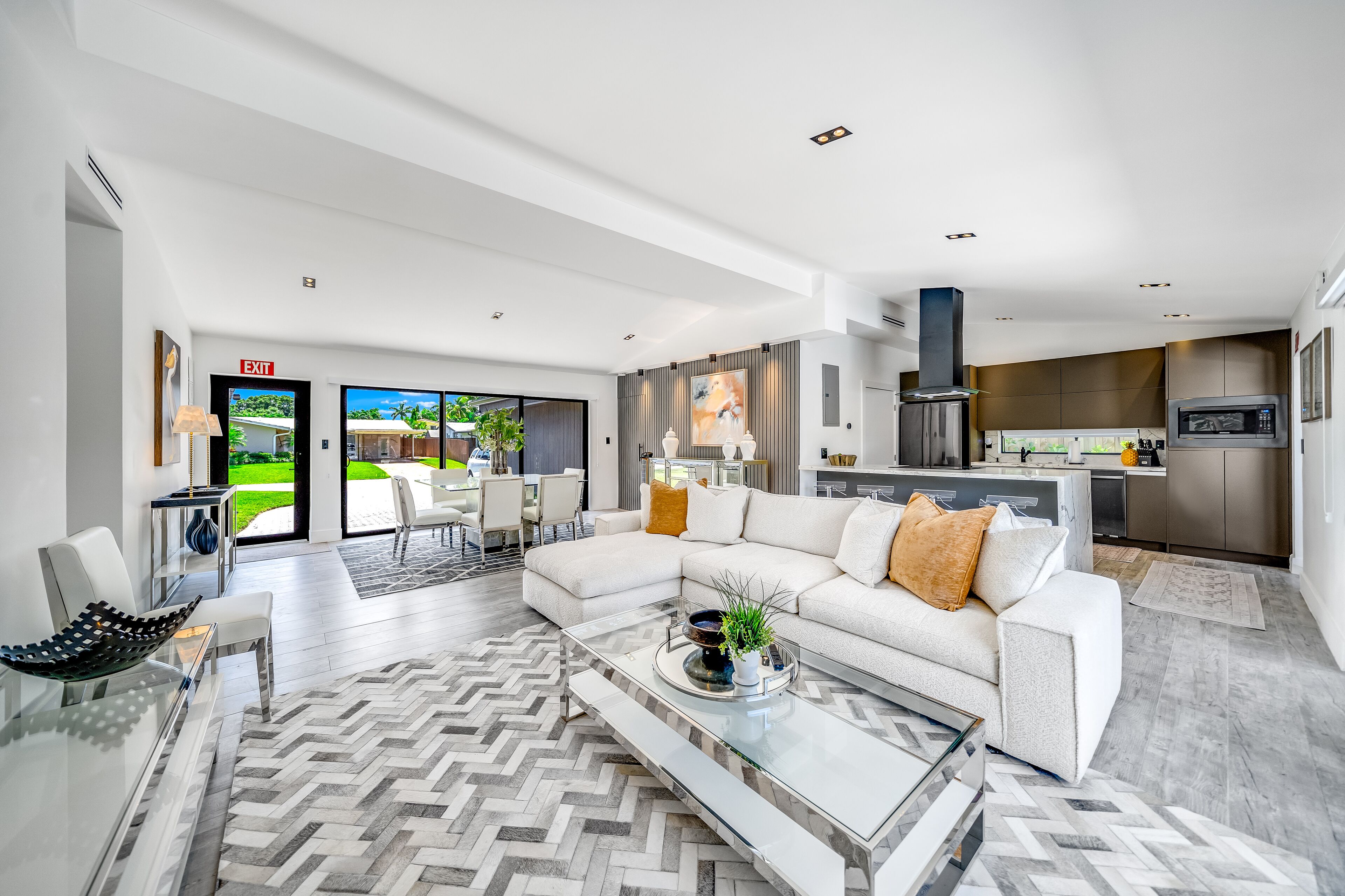 A modern living room with a glass coffee table, a white sofa, and a view to the outside.