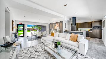 A modern living room with a glass coffee table, a white sofa, and a view to the outside.
