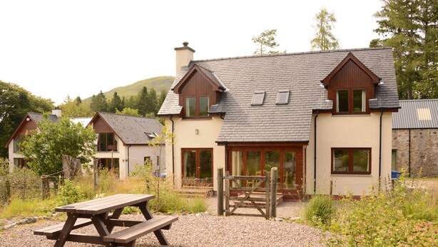 A rustic cabin with a wooden picnic table in front, surrounded by gravel and greenery. - Shepherds Rest (Fort William)