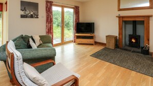 A living room with a green sofa, a television, a fireplace, and a large window with curtains. - Shepherds Rest (Fort William)