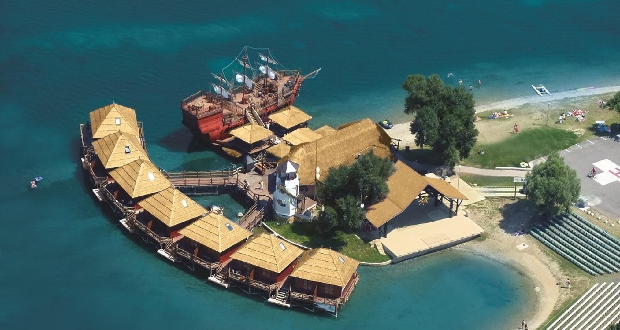 An aerial view of a waterfront property with multiple overwater bungalows, a central building, and a beach area.